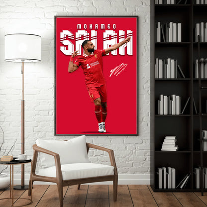Framed poster of a soccer player in a red uniform on a wall in a room with a chair and bookshelf.